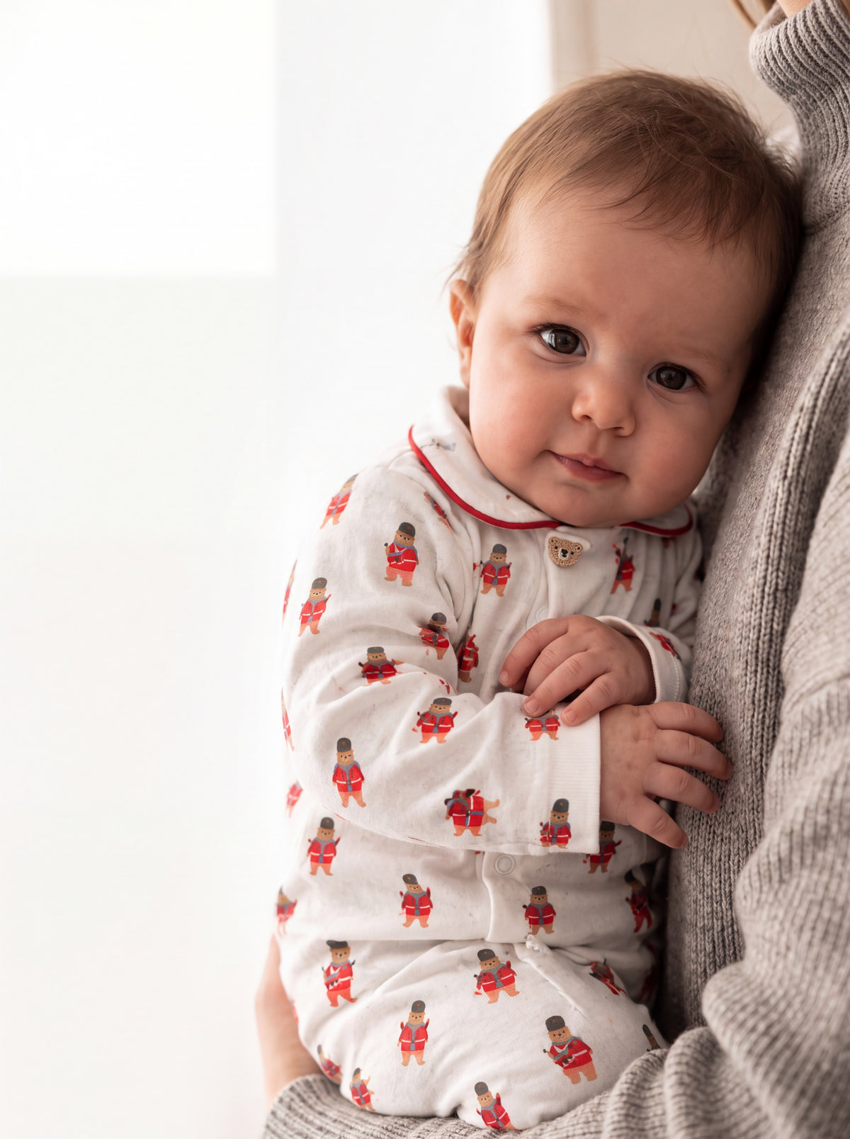 Baby sitting against an adult in the ivory guard bear sleepsuit