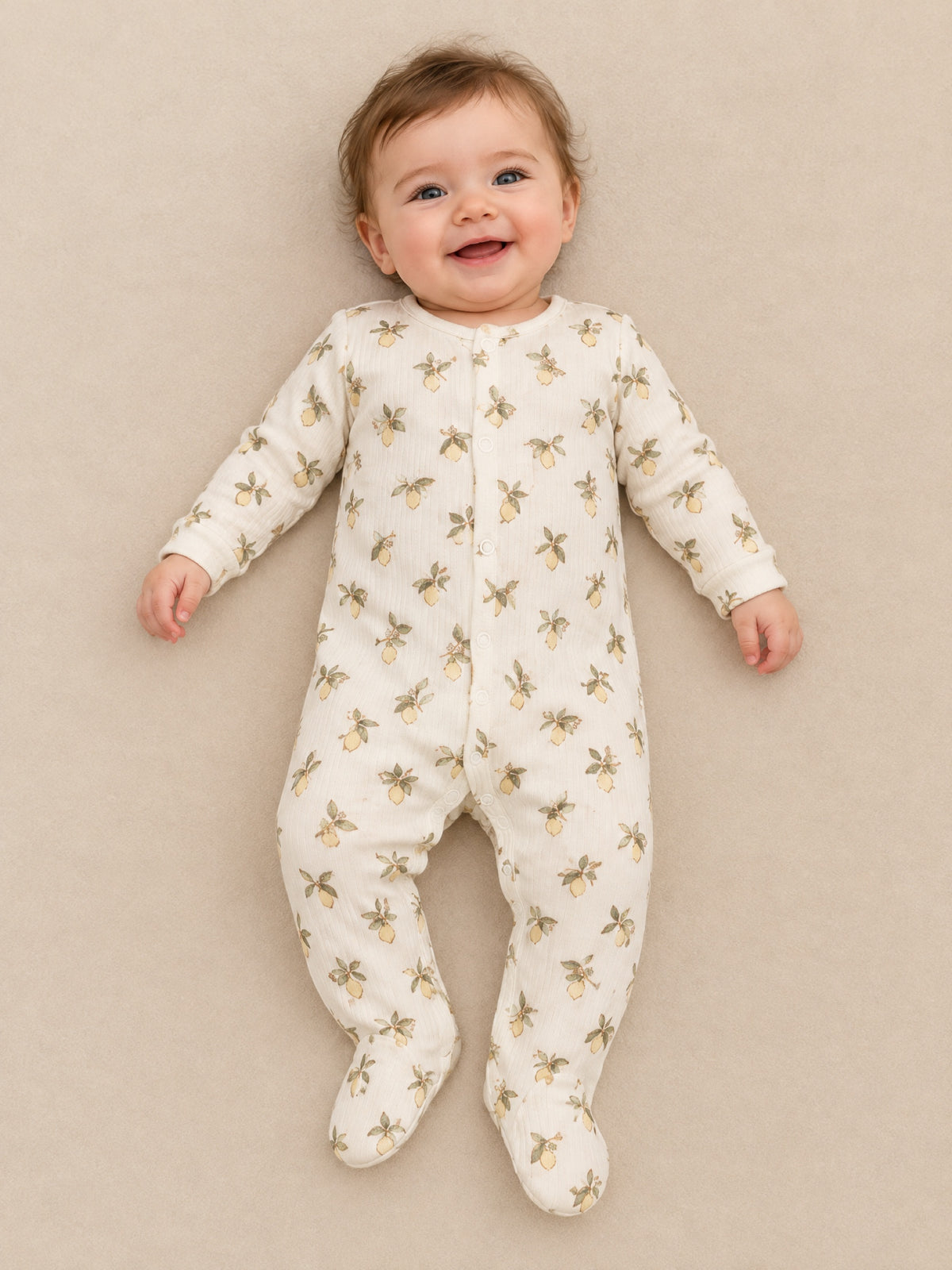 Baby lying down in the ivory lemon print footed sleepsuit