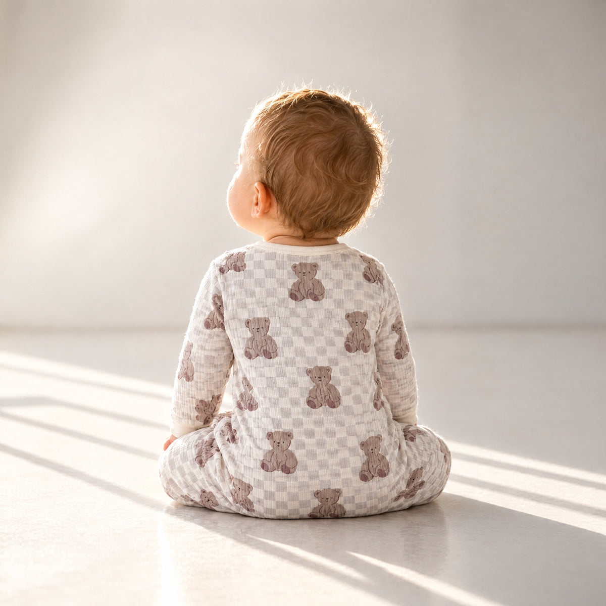 Baby sitting in the bear checkerboard sleepsuit, back view